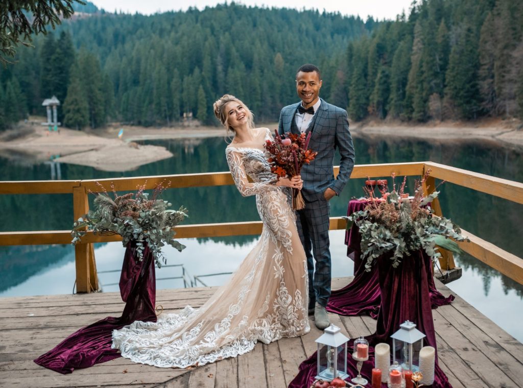 newly married couple standing on a dock decorated with flowers and cancles